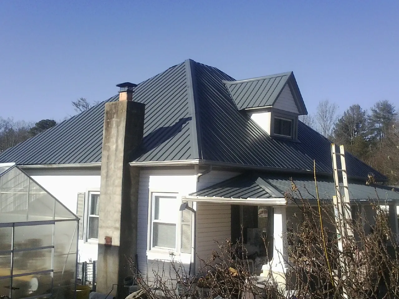 Dark blue standing seam metal roof on a white farmhouse with dormer — Slate & Tile Roof Repair by Roofing Brothers in Elliston