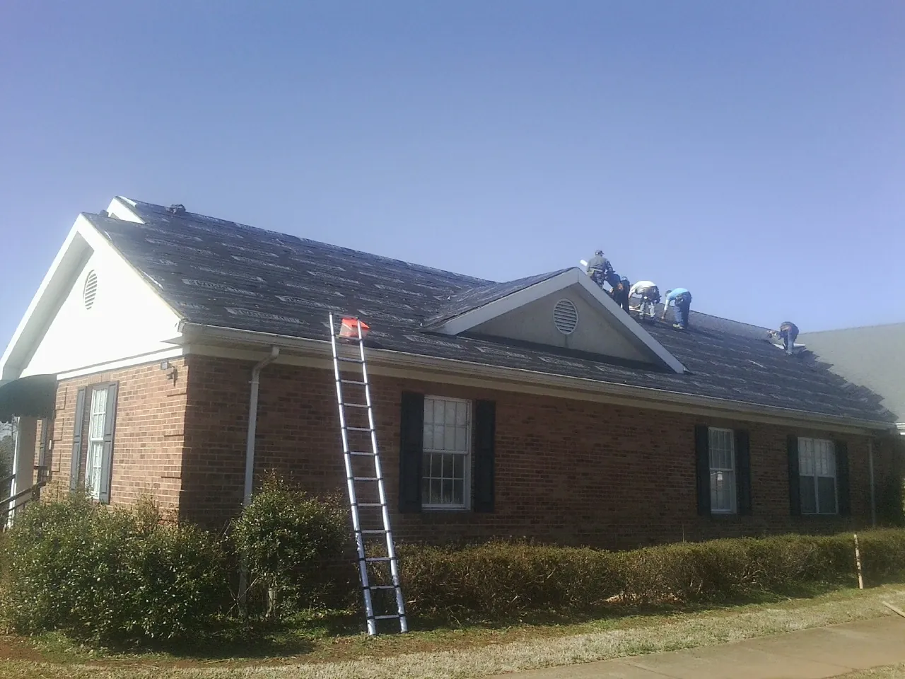 Crew tearing shingles off a brick ranch roof with a ladder set — Metal Roof Repair work by our crew in Elliston