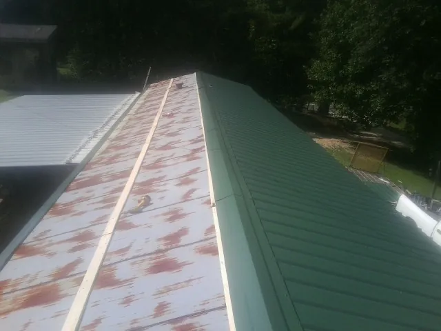 Old rusted panels beside newly installed green metal roofing — Wind Damage Roof Repair by Roofing Brothers in Elliston